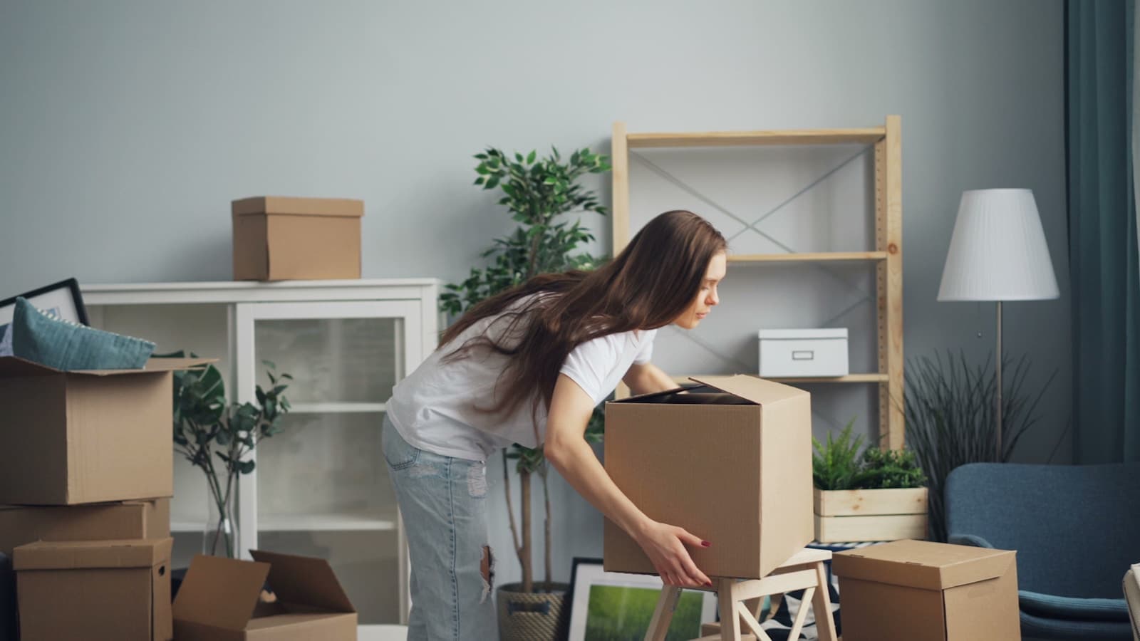 Woman carrying moving boxes across a sunlit living room
